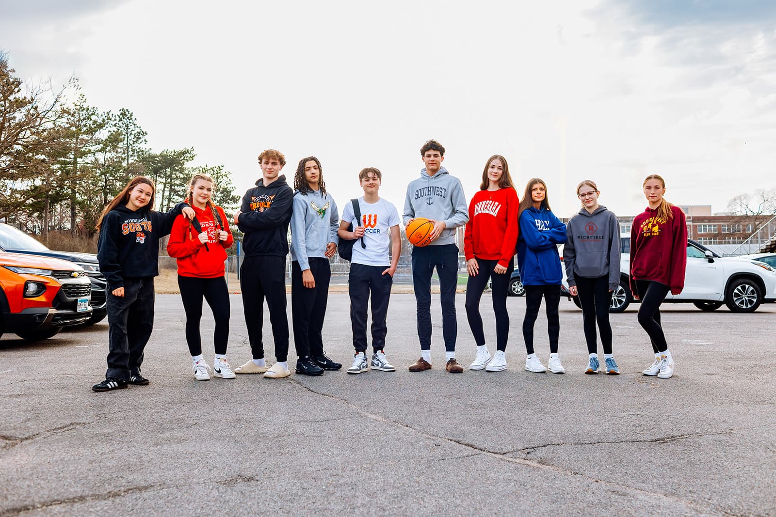 Group of ten high school driver's education students standing together in parking lot wearing college sweatshirts